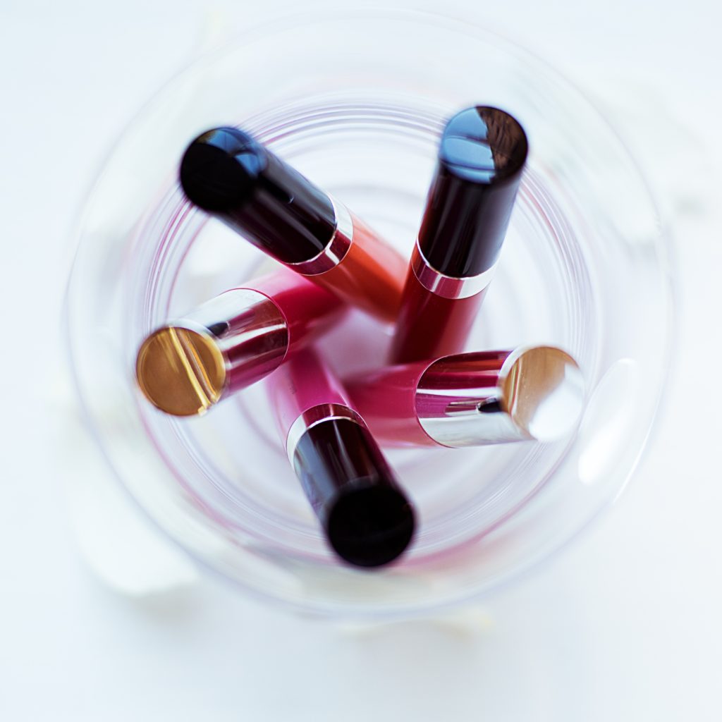 Fünf Lipglosse in kräftigen Rot- und Pinktönen stehend in einem Glas.