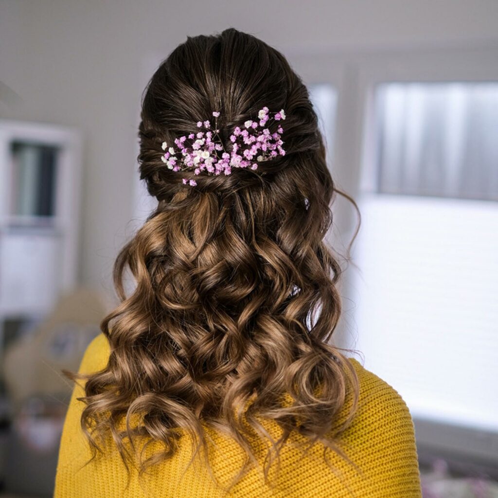 Halboffenes, gelocktes Hairstyling. Die Braut trägt rosafarbenes Schleierkraut als Schmuck.