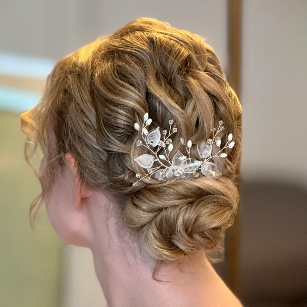 Ein tiefer Dutt an dunkelblondem Haar mit gelocktem Hinterkopf und Haarschmuck.